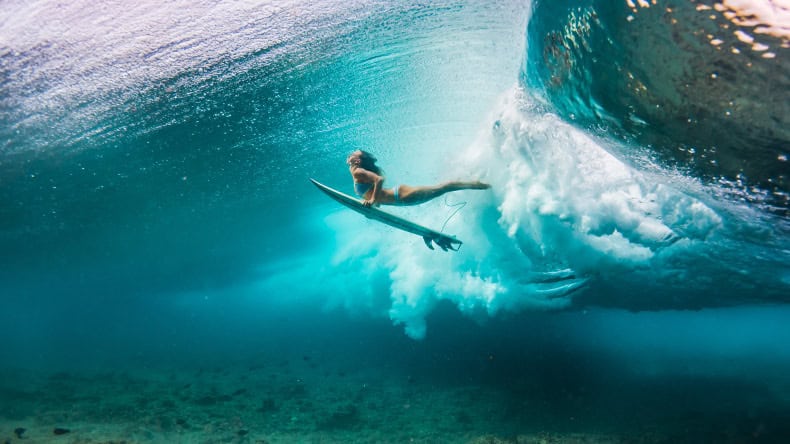 Frau im Bikini macht einen Duck Dive mit dem Surfbrett unter den Wellen