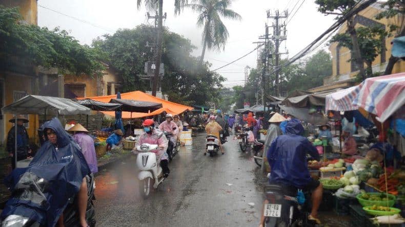 Mit Regencapes schützen sich die Rollerfahrer vor dem Regen während sie auf dem Markt einkaufen
