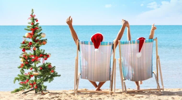 Zwei Menschen sitzen mit Nikolausmützen am Strand neben einem Weihnachtsbaum
