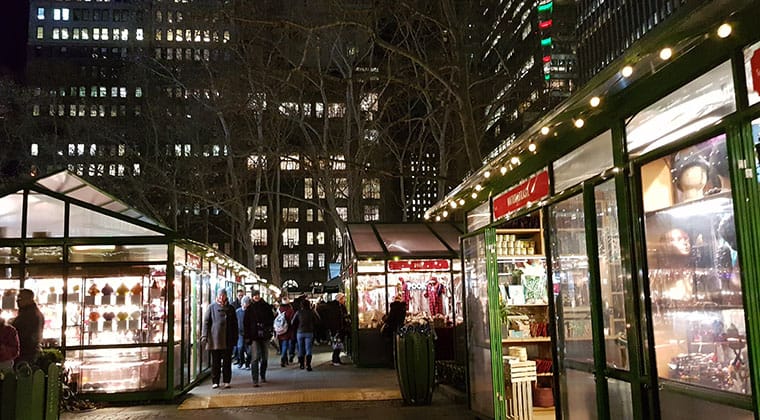 Blick auf den Weihnachtsmarkt im Bryant Park am Abend mit hell erleuchteten und festlich geschmückten Buden, New York, USA