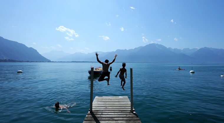Kinder springen bei strahlendem Sonnenschein von einem Steg in den Genfer See