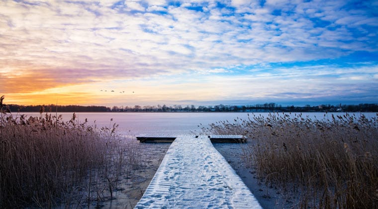 Sonnenaufgangsstimmung im Winter an einem Verschneiten See in Masuren, Polen.