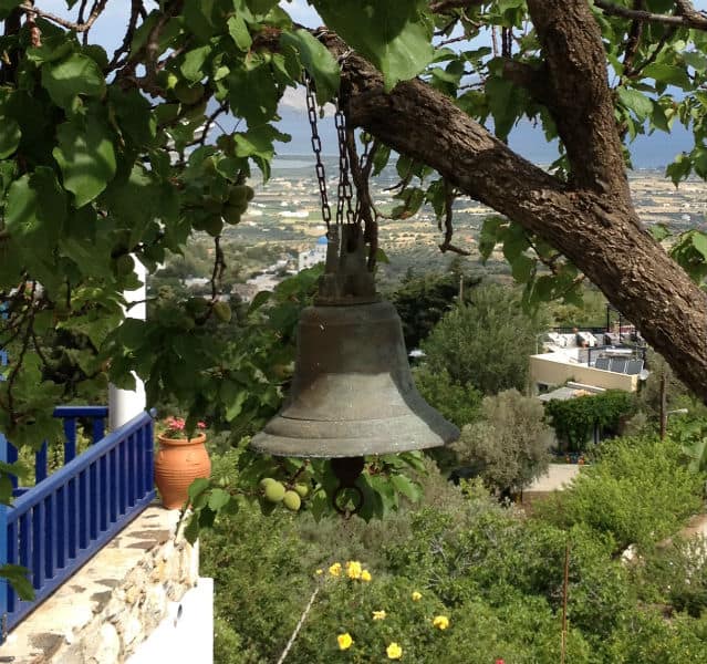 Eine Glocke hängt an einem Baum, im Hintergrund liegt ein Dorf
