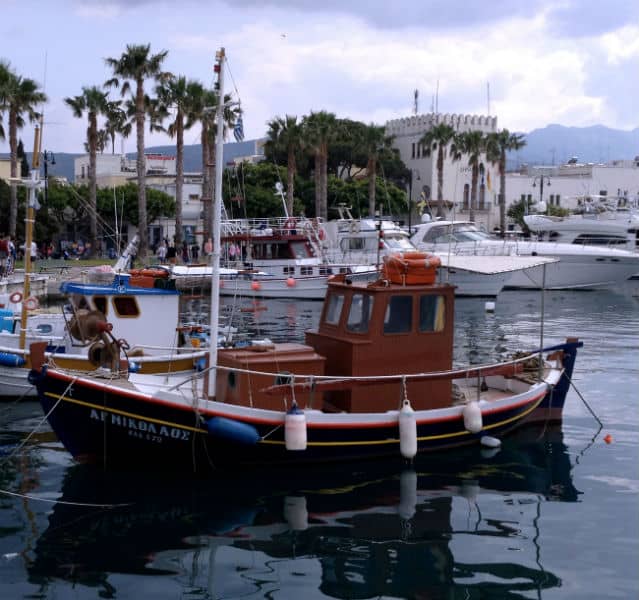 Ein rotes Boot liegt im Hafen von Kos, dahinter weitere Boote und Touristen