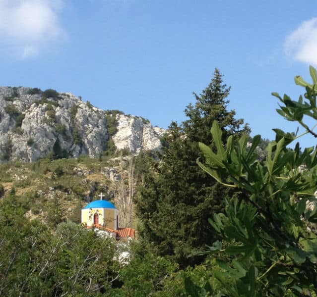 Kleine Kirche auf einem Berg, im Vordergrund Bäume und Büsche