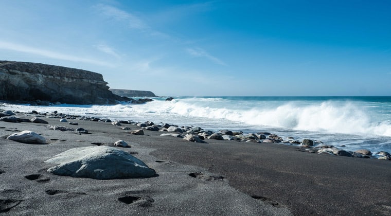 Blick auf einen schwarzen Strand mit Wellengang auf der Kanareninsel Fuerteventura.