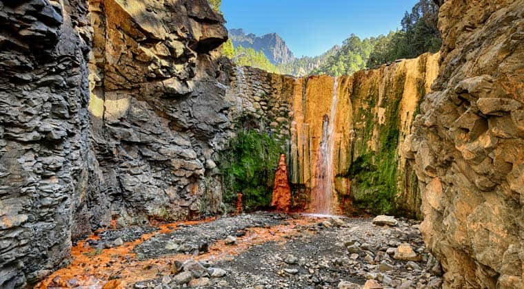 Blick auf die Cascada de Colores – der orangerot schimmernde Wasserfall an einer Felswand aus Vulkangestein