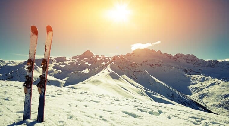 Skibretter stecken im Schnee und im Hintergrund sieht man die schneebedeckten Berge mit untergehender Sonne