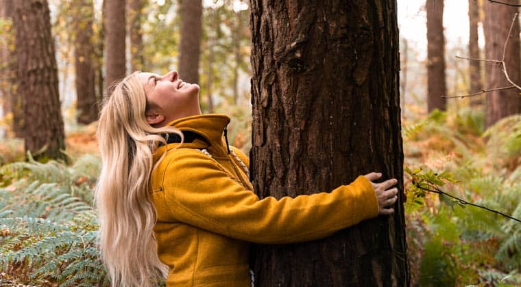 Eine Frau die sich an einen Baum im Wald schmiegt und zur Baumkrone hinaufschaut