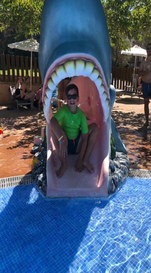 Kind sitzt im Maul einen Plastikhais im Kinderpool im Beach Club Font de Sa Cala