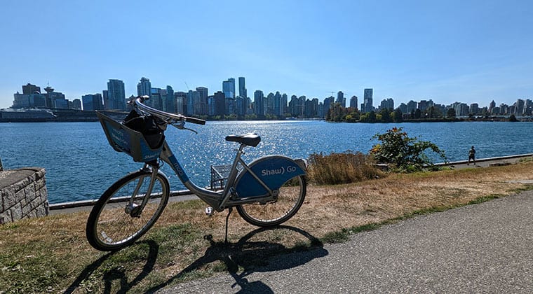 Blick auf ein Fahrrad, das an einer Uferpromenade steht, mit Skyline von Vancouver im Hintergrund, British Columbia, Kanada