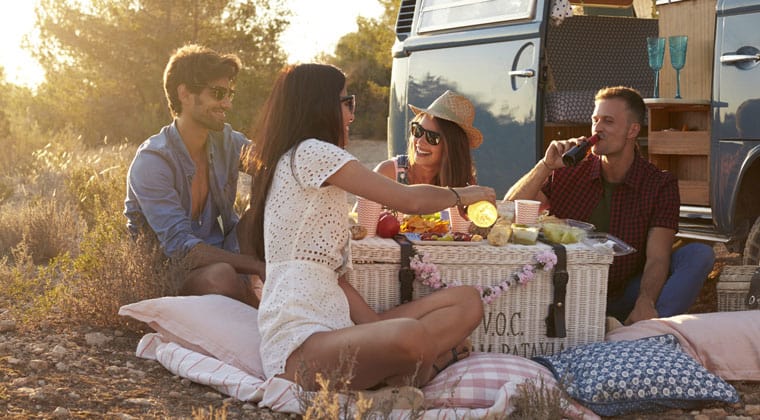 Vier Freunde bei einem gemütlichen Picknick, direkt vor ihrem Camper bei Sonnenuntergang