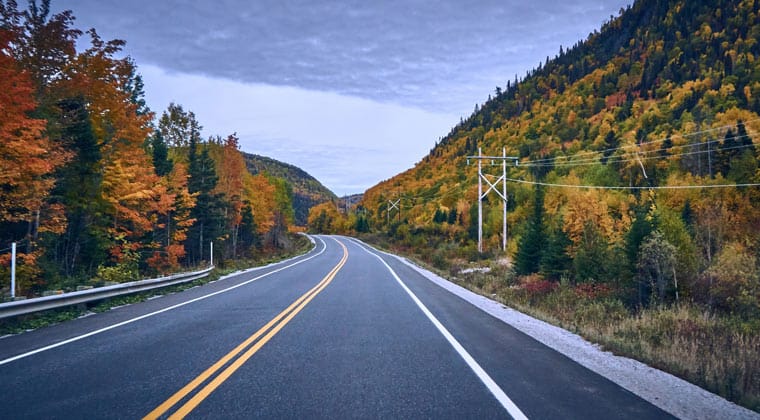 Eine Straße in Kanada zur Zeit des Indian Summers. Die Laubbäume entlang der Straße sind gefärbt in den typischen Farben rot-gelb und orange.