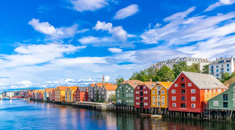 Blick auf die bunten Häuser auf Holzpfählen am Ufer des Fluss Nidelva in der Stadt Trondheim in Norwegen.