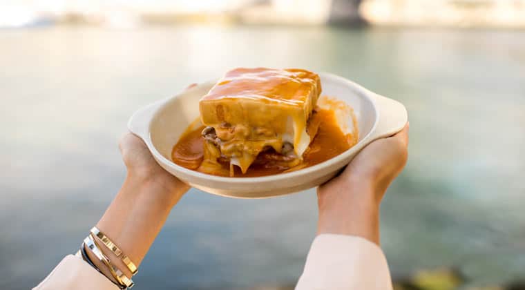 Ein Teller mit der Spezialität aus Porto in Portugal: Francessinha. Die Zutaten sind Toastbrot, Kochschinken, Linguiça, gebratenes Rindfleisch und geschmolzener Käse plus Tomatensoße.