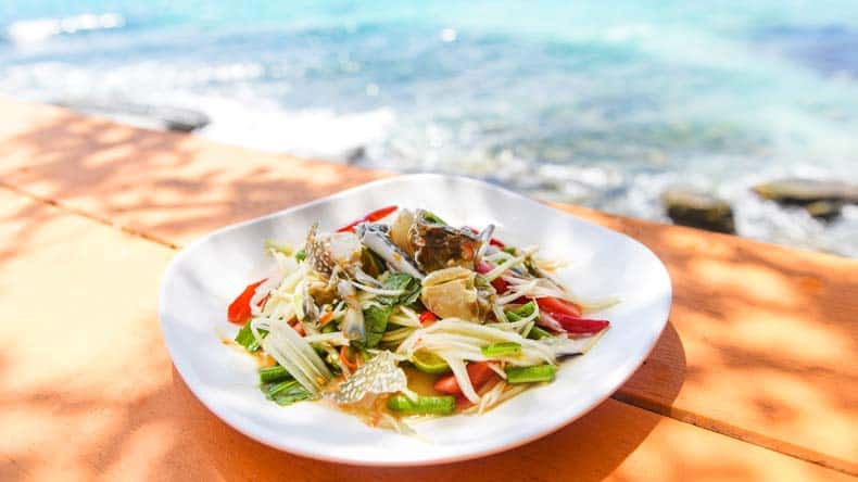 Essteller mit thailändischem Salat und Strand im Hintergrund