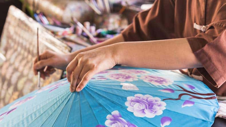 Türkisfarbener Papierschirm, der mit bunten Blumen bemalt wird, Chiang Mai, Thailand