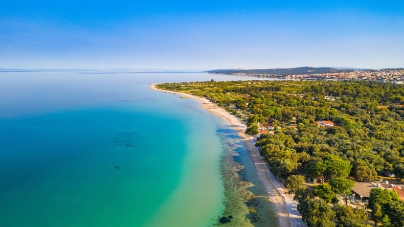 Blick auf einen langen Strandabschnitt mit hellem Kieselstrand und türkisfarbenem Wasser auf der Insel Pag, Kroatien