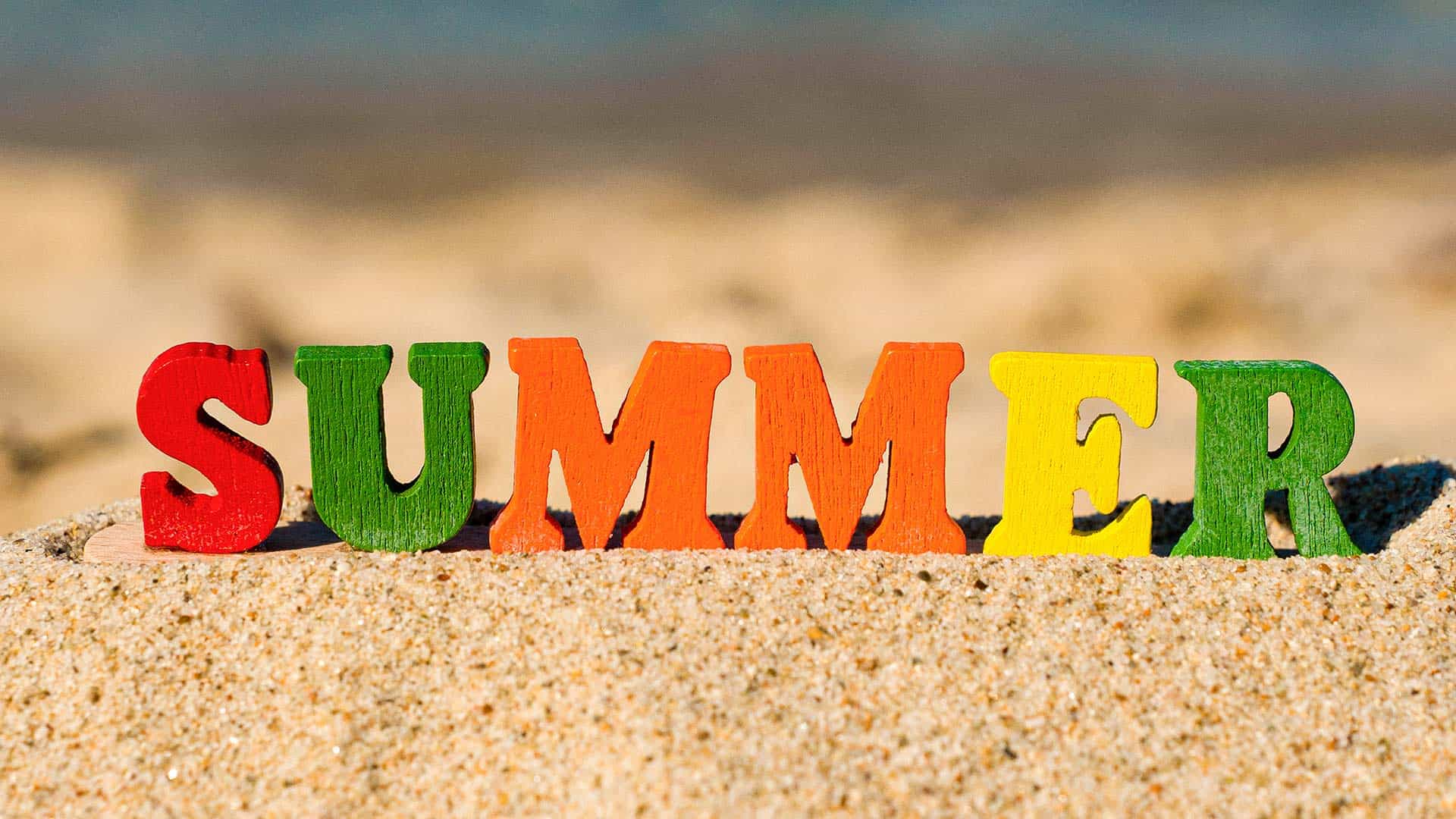 Bunte Holzbuchstaben, die das Wort „Summer“ (Sommer) bilden, liegen auf einem schönen Sandstrand
