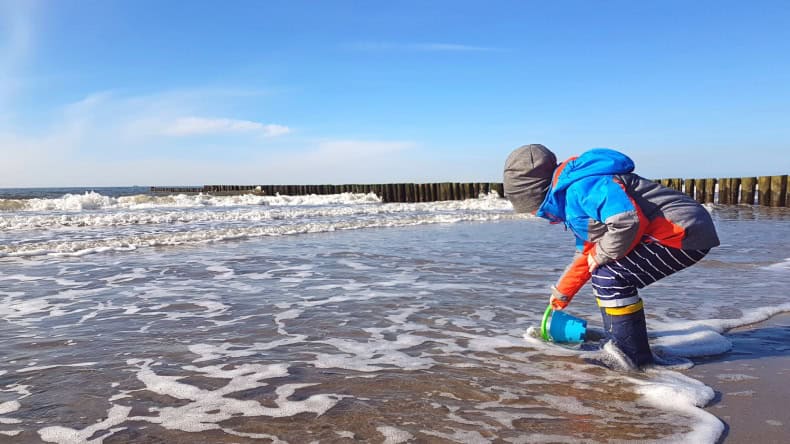 Kleiner Junge in Gummistiefeln spielt am Meer.
