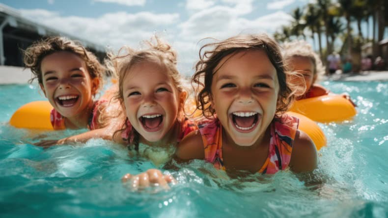 Vier lachende Kleinkinder im Pool mit gelben Schwimmreifen, Urlaub mit Kleinkind