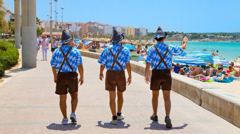 Blick auf drei Männer in bayrischer Tracht an der Strandpromenade am Ballermann, Strand, türkisfarbenes Meer, Mallorca, Balearen