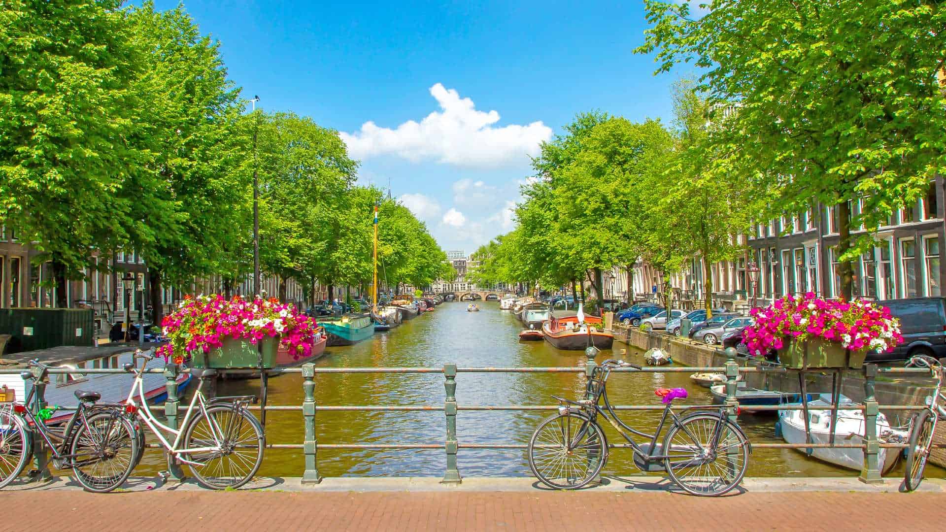 Blick auf eine typische Gracht mit Booten und eine Brücke mit Fahrrädern in Amsterdam.