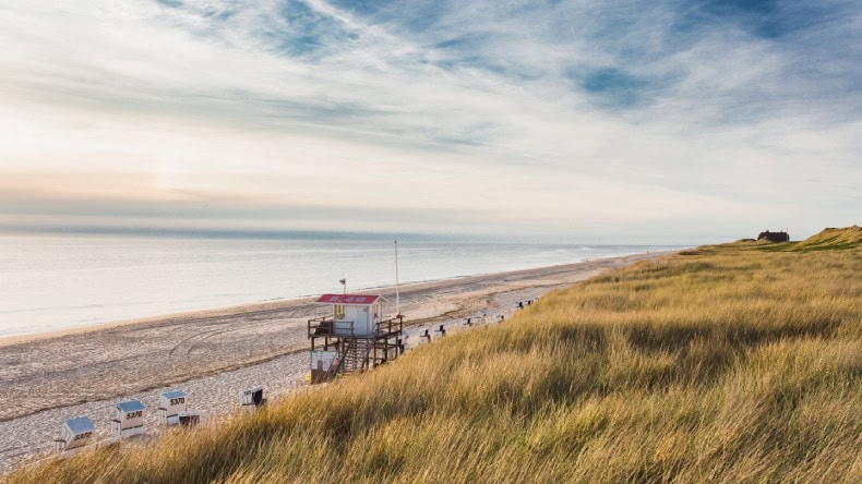 Blick auf einen langen Sandstrand, einen Rettungsturm und Dünen in Rantum, Sylt, Deutschland, Kurtaxe