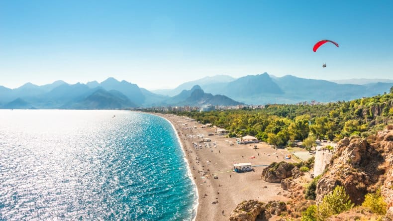 Blick auf den Strand von Antalya, brauner Sand, blaues Meer, Berge, Paraglider, Antalya, Türkei