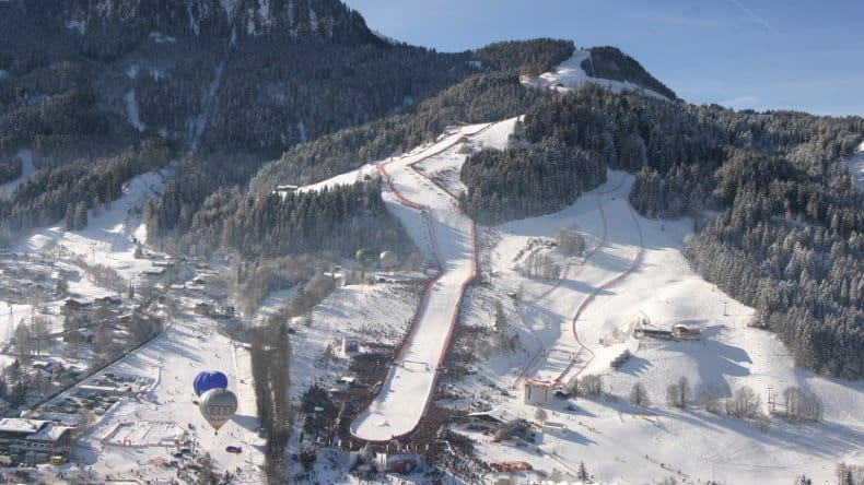 Blick auf die Rennstrecke Hahnenkamm im Skigebiet Kitzbühel, Schnee, Berge mit Nadelbäumen, blauer Himmel, Österreich