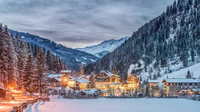 Blick auf ein verschneites, erleuchtetes Dorf in den Bergen in der Abenddämmerung
