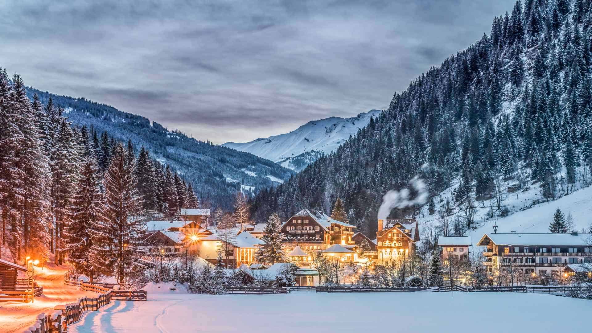 Blick auf ein verschneites, erleuchtetes Dorf in den Bergen in der Abenddämmerung