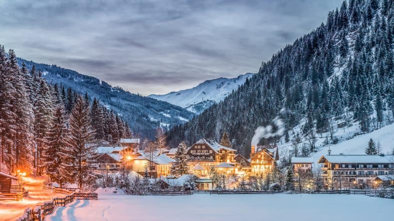 Blick auf ein verschneites, erleuchtetes Dorf in den Bergen in der Abenddämmerung