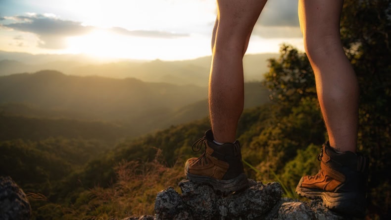 Wanderer in Wanderschuhen steht auf einem Felsen und guckt in die Natur.