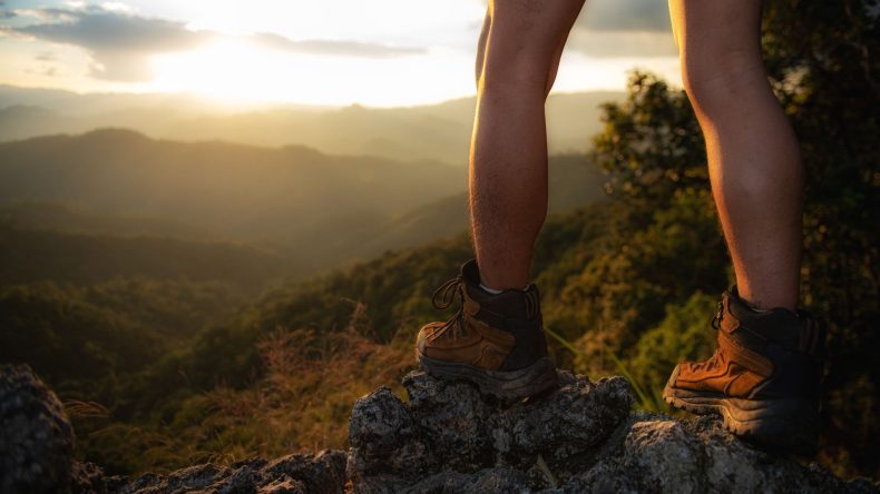 Wanderer in Wanderschuhen steht auf einem Felsen und guckt in die Natur.