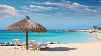 Blick auf einen hellen Sandstrand mit Strohsonnenschirm und zwei Sonnenliegen, türkisfarbenes Meer, Ägypten