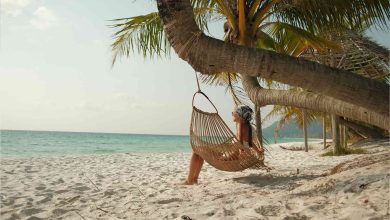 Eine Frau entspannt in einem Hängesessel unter Palmen an einem tropischen Sandstrand