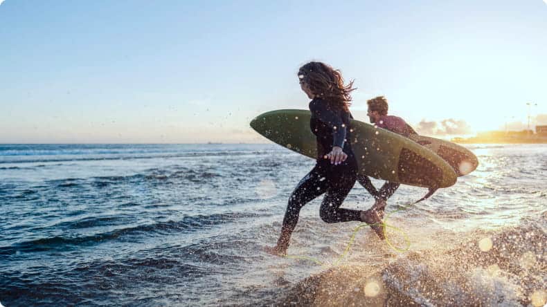 Paar springt ins Wasser mit Surfbrettern in der Hand