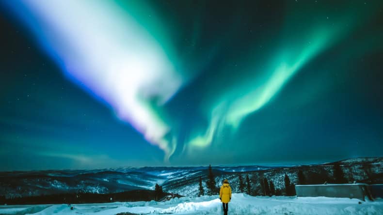 Eine Frau steht auf einem schneebedeckten Hügel und schaut auf Polarlichter , Fairbanks, Alaska