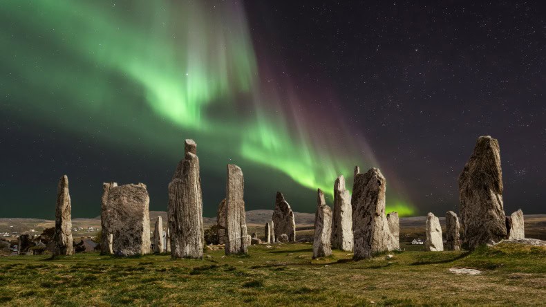 Blick auf einen Steinkreis bei Nacht in Schottland, darüber violett-grüne Polarlichter