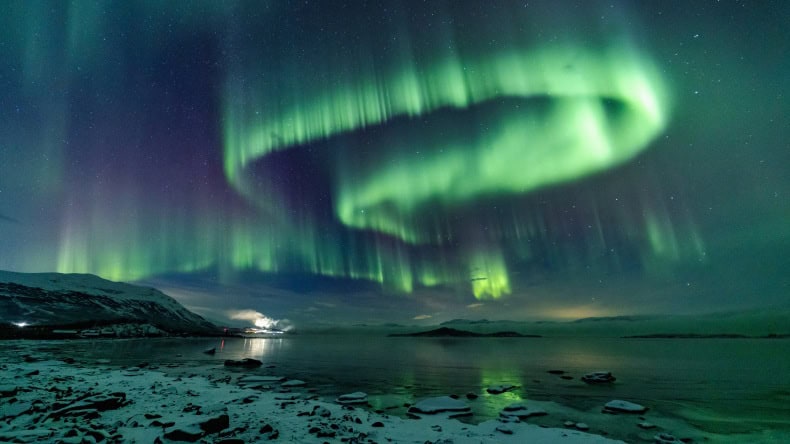 Blick auf eine grün-violette Aurora borealis über dem Torneträsk-See in Schweden