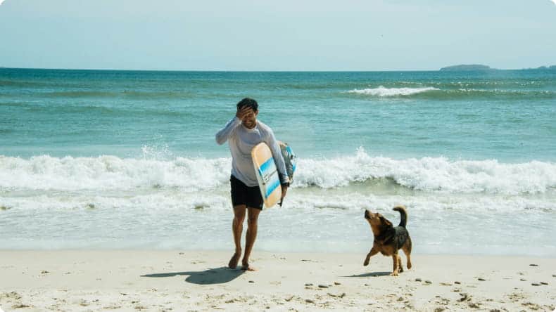 Mann mit Surfboard und Hund am Strand