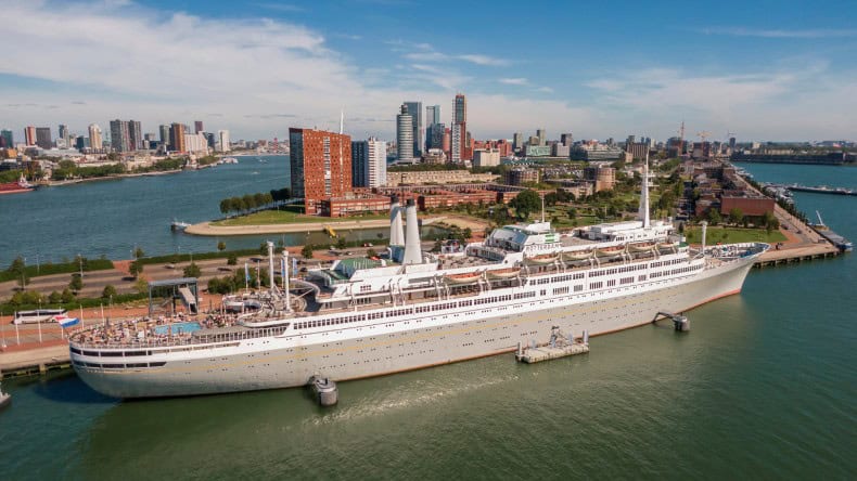 Luftaufnahme des vor Katendrecht liegenden Frachtschiffs SS Rotterdam mit der Skyline von Hochhäusern im Hintergrund
