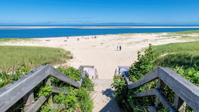 Blick auf einen Strand in Cape Cod, heller Sand, blaues Meer, Holztreppe, wenige Menschen, Massachusetts, USA