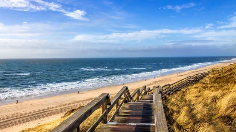 Blick auf den Strand bei Wenningstedt, blaues Meer, Wellen, langer Sandstrand, Dünen, wenige Menschen, Holztreppe, Sylt, Deutschland