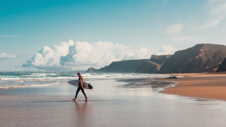 Atlantik, Meer, Strand, Felsen im Hintergrund, Surferin mit Board