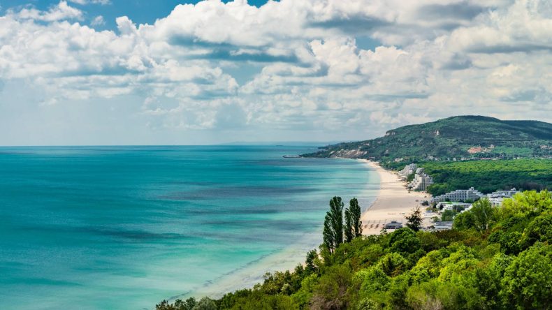 Blick auf einen langen Sandstrand bei Albena, heller Sand, türkis-blaues Meer, grün bewachsenes Hinterland, Hotelgebäude