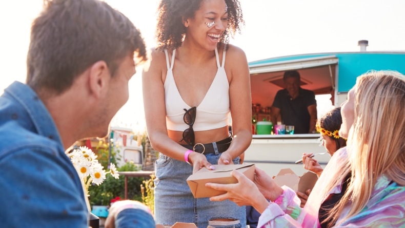Eine Gruppe von jungen Menschen vor einem Foodtruck auf einem Musikfestival.